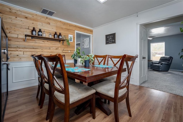 dining space with wood-type flooring, wooden walls, and ornamental molding