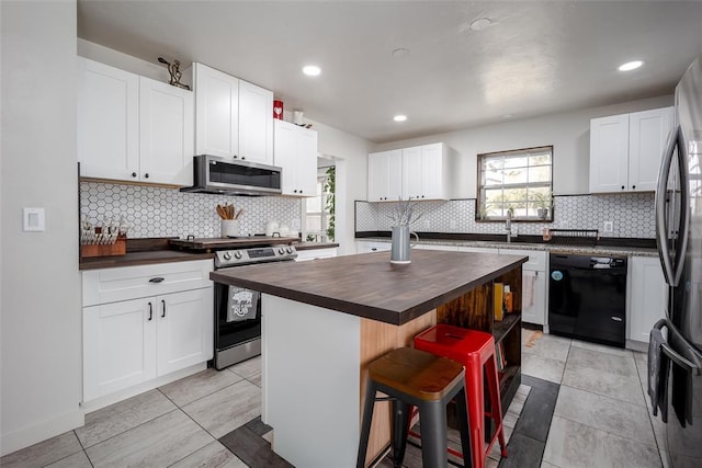 kitchen with white cabinets, stainless steel appliances, a center island, and butcher block countertops