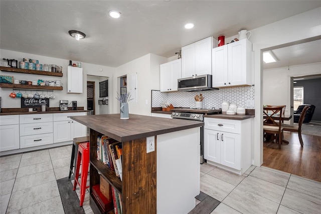 kitchen featuring wooden counters, appliances with stainless steel finishes, white cabinetry, a center island, and decorative backsplash