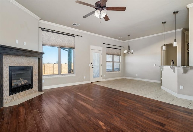 unfurnished living room featuring a healthy amount of sunlight, ornamental molding, a tiled fireplace, and light wood-type flooring