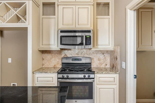 kitchen with light stone countertops, appliances with stainless steel finishes, backsplash, and cream cabinets