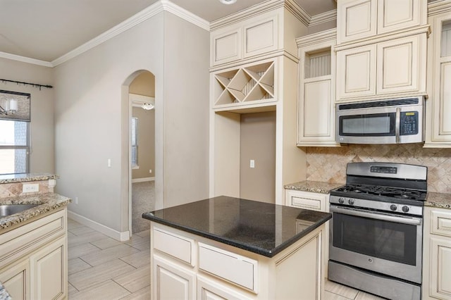 kitchen with appliances with stainless steel finishes, dark stone countertops, backsplash, ornamental molding, and cream cabinets