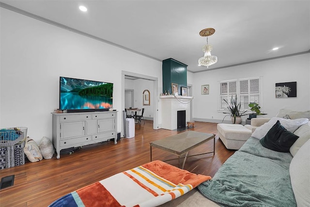 living room with crown molding, a brick fireplace, an inviting chandelier, and dark hardwood / wood-style flooring