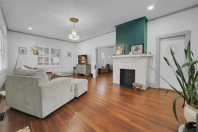 living room with wood-type flooring, a brick fireplace, an inviting chandelier, and crown molding