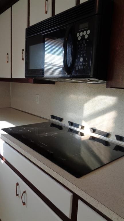 kitchen featuring backsplash, black appliances, and white cabinets