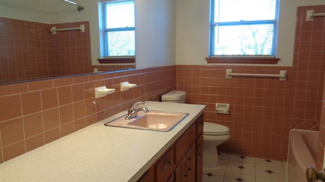 bathroom with tile patterned floors, toilet, tile walls, vanity, and a bathtub