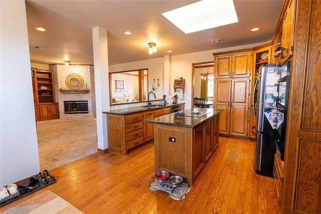 kitchen with sink, a center island, stainless steel refrigerator, a fireplace, and light hardwood / wood-style floors