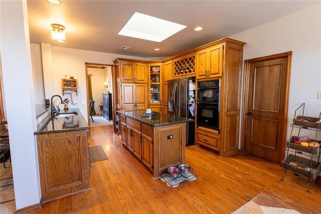 kitchen featuring light hardwood / wood-style flooring, sink, a skylight, and black appliances