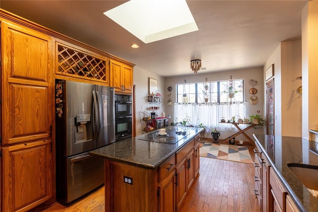 kitchen featuring a skylight, dark stone countertops, light wood-type flooring, and black appliances