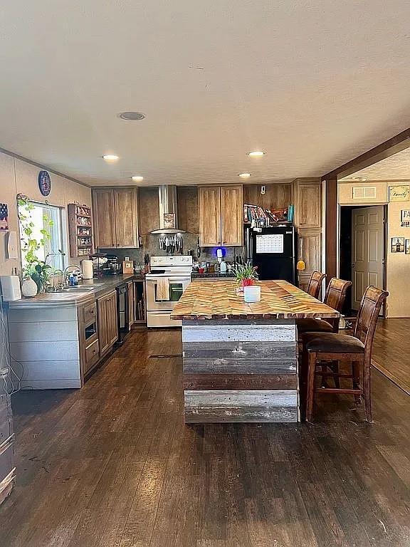 kitchen featuring wall chimney exhaust hood, a breakfast bar area, wooden counters, dark hardwood / wood-style flooring, and black appliances