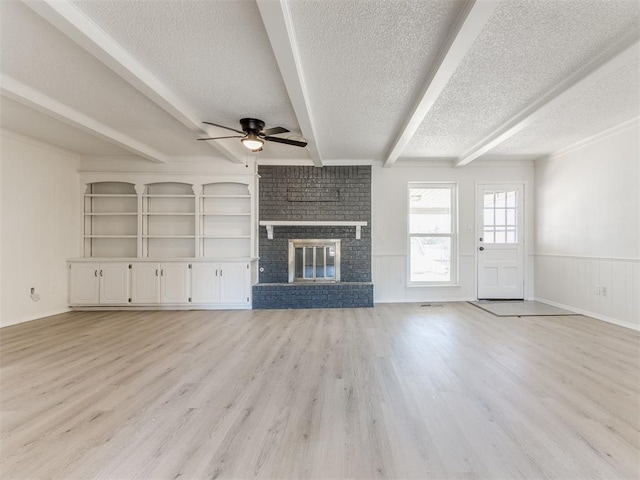 unfurnished living room featuring a fireplace, beam ceiling, ceiling fan, light hardwood / wood-style floors, and a textured ceiling