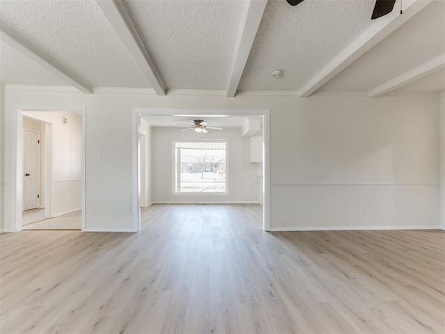 unfurnished room featuring ceiling fan, beam ceiling, a textured ceiling, and light wood-type flooring