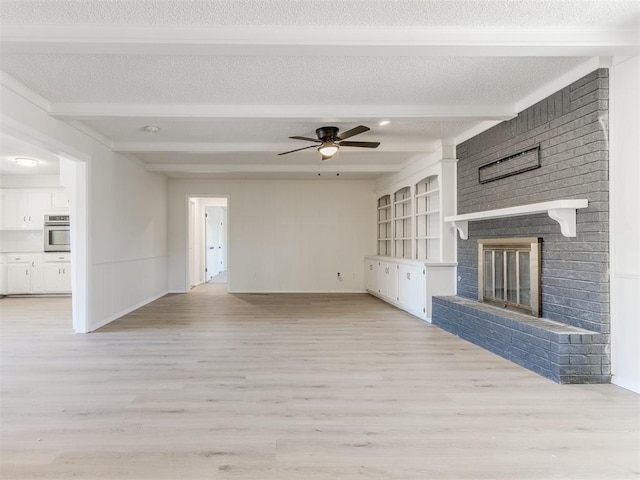 unfurnished living room with a brick fireplace, a textured ceiling, light wood-type flooring, beamed ceiling, and ceiling fan