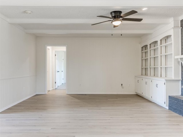 empty room featuring ceiling fan, beam ceiling, light hardwood / wood-style floors, a textured ceiling, and a brick fireplace