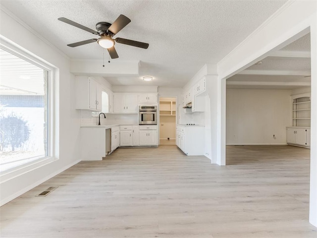 kitchen featuring sink, stainless steel oven, a textured ceiling, light hardwood / wood-style floors, and white cabinets