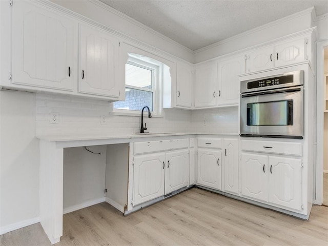 kitchen with sink, white cabinetry, stainless steel oven, tasteful backsplash, and light hardwood / wood-style flooring