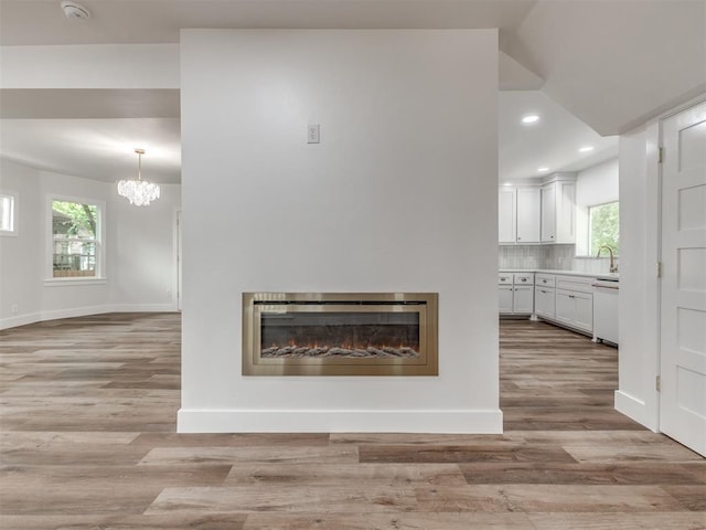 unfurnished living room with sink, a notable chandelier, vaulted ceiling, and light wood-type flooring