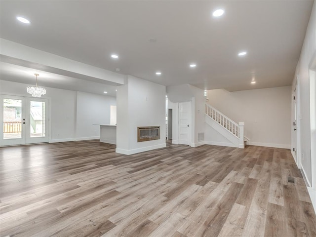 unfurnished living room featuring an inviting chandelier, french doors, and light wood-type flooring