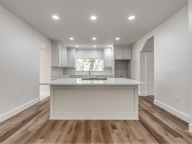 kitchen featuring white cabinets, a center island, light hardwood / wood-style floors, and backsplash