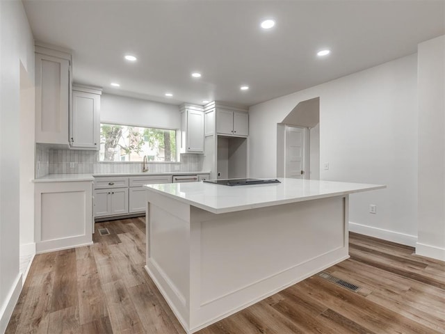 kitchen with a kitchen island, sink, light hardwood / wood-style flooring, and decorative backsplash