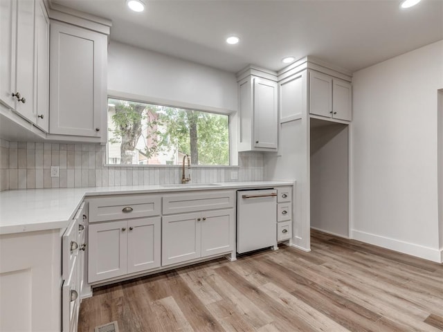 kitchen with sink, dishwasher, white cabinetry, tasteful backsplash, and light wood-type flooring