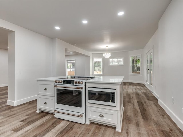 kitchen with stainless steel microwave, light hardwood / wood-style floors, high end white range, and white cabinets