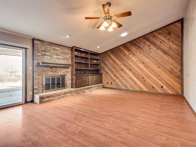 unfurnished living room with ceiling fan, a fireplace, wooden walls, and light hardwood / wood-style floors