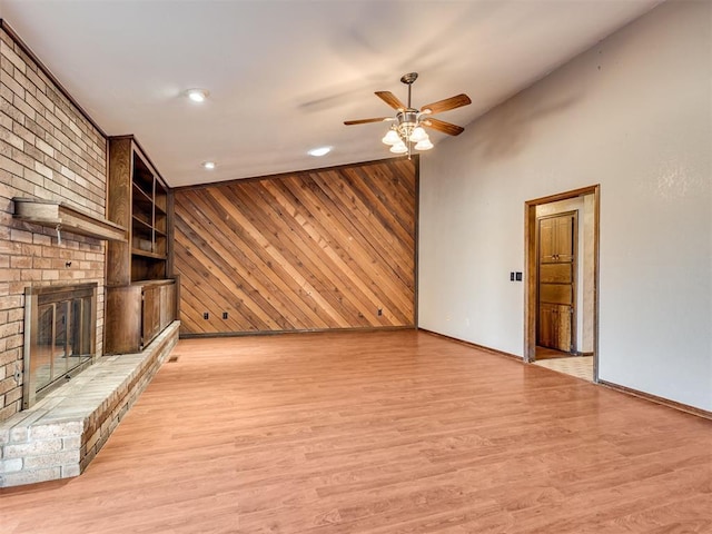 unfurnished living room featuring light hardwood / wood-style flooring, built in features, ceiling fan, wooden walls, and a fireplace