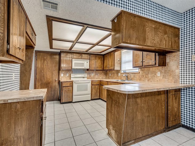 kitchen featuring light tile patterned flooring, white appliances, kitchen peninsula, and sink