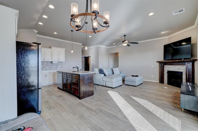 living room featuring a stone fireplace, sink, ornamental molding, ceiling fan with notable chandelier, and light hardwood / wood-style floors