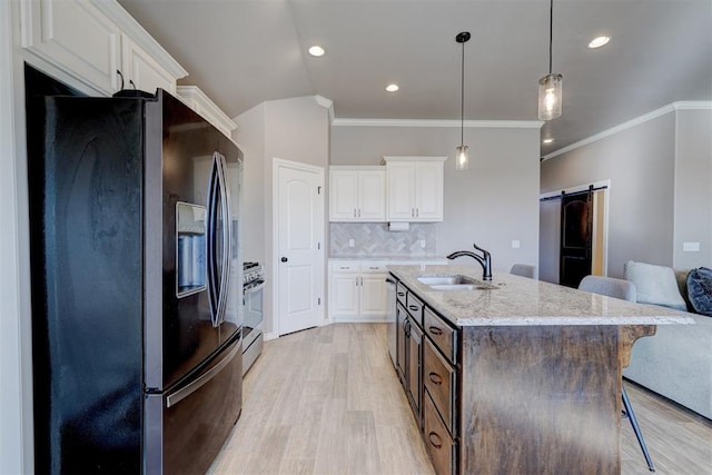 kitchen with sink, appliances with stainless steel finishes, white cabinetry, light stone countertops, and a barn door