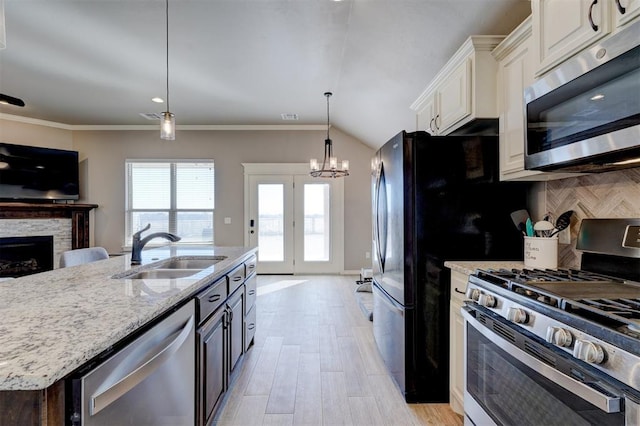 kitchen featuring appliances with stainless steel finishes, pendant lighting, a fireplace, white cabinetry, and sink