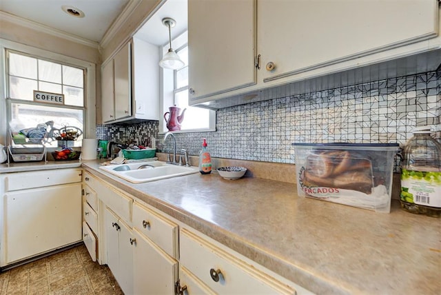 kitchen with sink, white cabinetry, hanging light fixtures, ornamental molding, and decorative backsplash