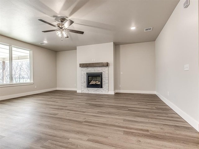 unfurnished living room with hardwood / wood-style flooring, a stone fireplace, and ceiling fan