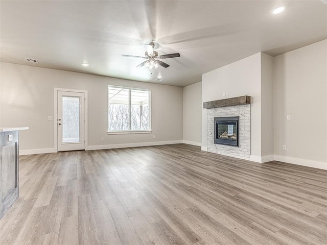 unfurnished living room with ceiling fan, a stone fireplace, and light wood-type flooring