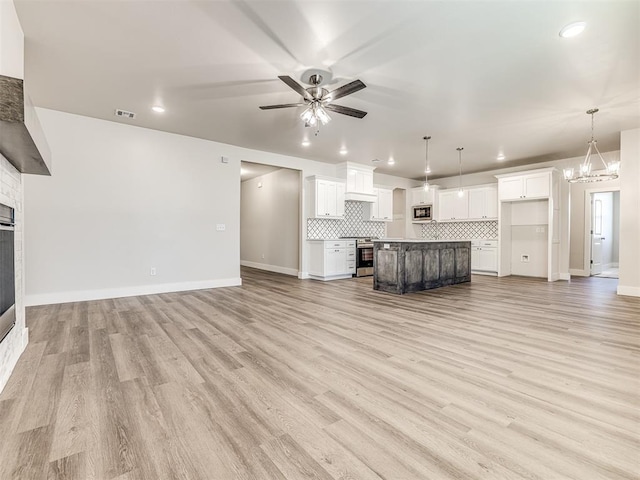 unfurnished living room featuring a large fireplace, ceiling fan with notable chandelier, and light hardwood / wood-style floors