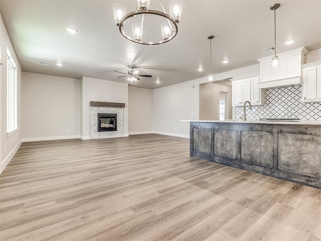 kitchen with gas stovetop, white cabinetry, pendant lighting, a fireplace, and light hardwood / wood-style floors