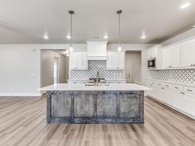 kitchen featuring black microwave, white cabinetry, sink, hanging light fixtures, and a center island with sink