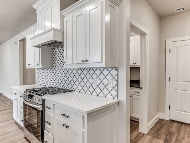 kitchen with light hardwood / wood-style flooring, light stone countertops, custom range hood, gas stove, and white cabinets