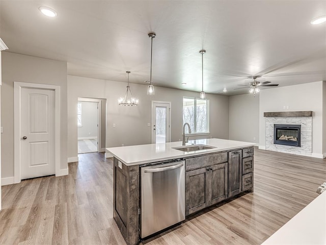 kitchen with decorative light fixtures, an island with sink, sink, stainless steel dishwasher, and light hardwood / wood-style flooring