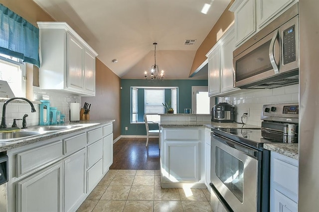 kitchen featuring vaulted ceiling, appliances with stainless steel finishes, decorative light fixtures, sink, and white cabinets