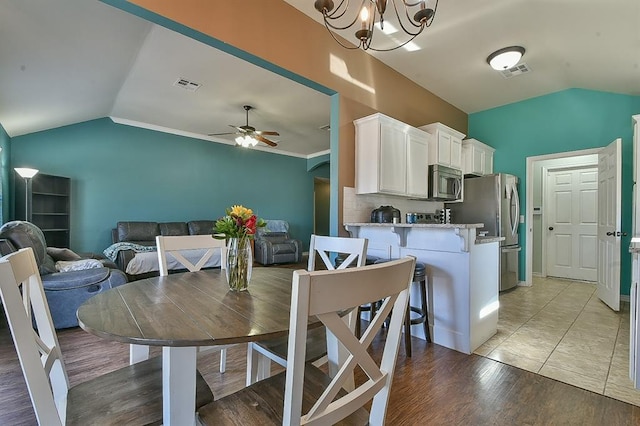 dining space with vaulted ceiling, ceiling fan with notable chandelier, and light hardwood / wood-style flooring