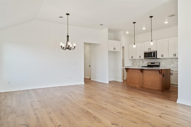 kitchen with stainless steel appliances, white cabinetry, pendant lighting, and a center island with sink