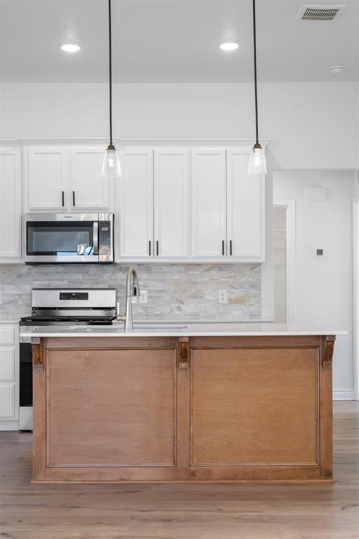 kitchen featuring pendant lighting, stainless steel appliances, a center island, white cabinets, and decorative backsplash