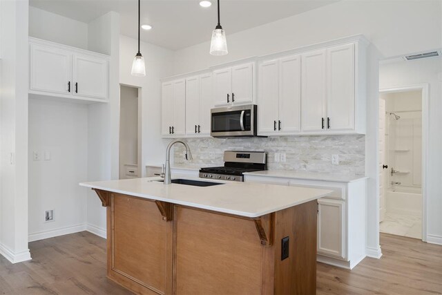 kitchen with white cabinetry, appliances with stainless steel finishes, an island with sink, and hanging light fixtures