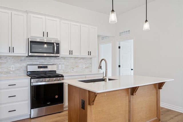 kitchen featuring stainless steel appliances, hanging light fixtures, a kitchen island with sink, and white cabinets