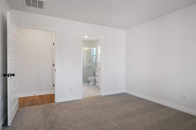 unfurnished bedroom featuring light colored carpet and ensuite bath