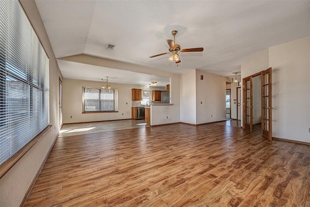 unfurnished living room with ceiling fan with notable chandelier, lofted ceiling, and light hardwood / wood-style floors