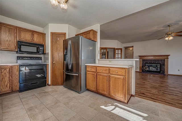 kitchen with a textured ceiling, a brick fireplace, kitchen peninsula, ceiling fan, and black appliances