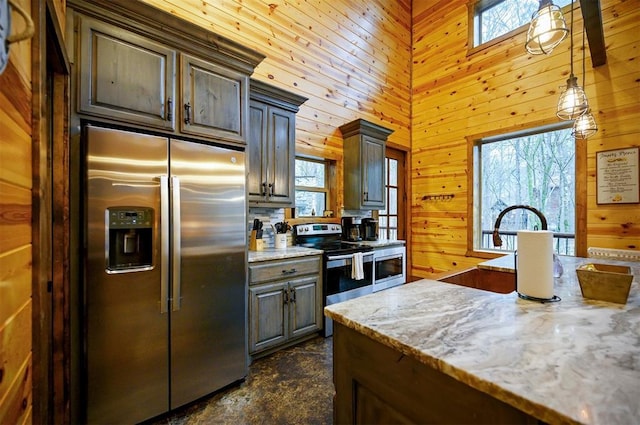 kitchen with wood walls, sink, hanging light fixtures, stainless steel appliances, and light stone countertops